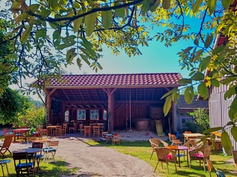 Melkhuske Schatteburg, Gemeinde Rhauderfehn, Ostfriesland Außenbereich eines Cafés oder Restaurants mit mehreren Tischen und Stühlen auf einer Wiese vor einem offenen Holzschuppen unter blauem Himmel