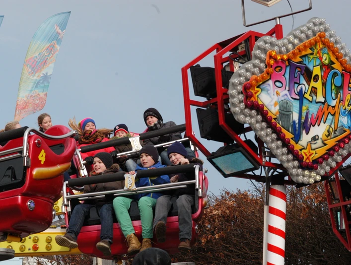 DSC_0002.JPG Menschen lachen und jubeln in bunten Sitzen einer aufregenden Jahrmarktfahrt bei sonnigem Wetter.