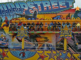 DSC_0811.JPG Menschen fahren auf einem bunten Jumpstreet-Fahrgeschäft, umgeben von leuchtenden Lichtern und Grafiken.