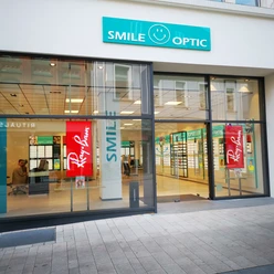 Ein modernes Augenoptikfachgeschäft mit großen Glasfenstern und leuchtendem Smile Optic Logo.