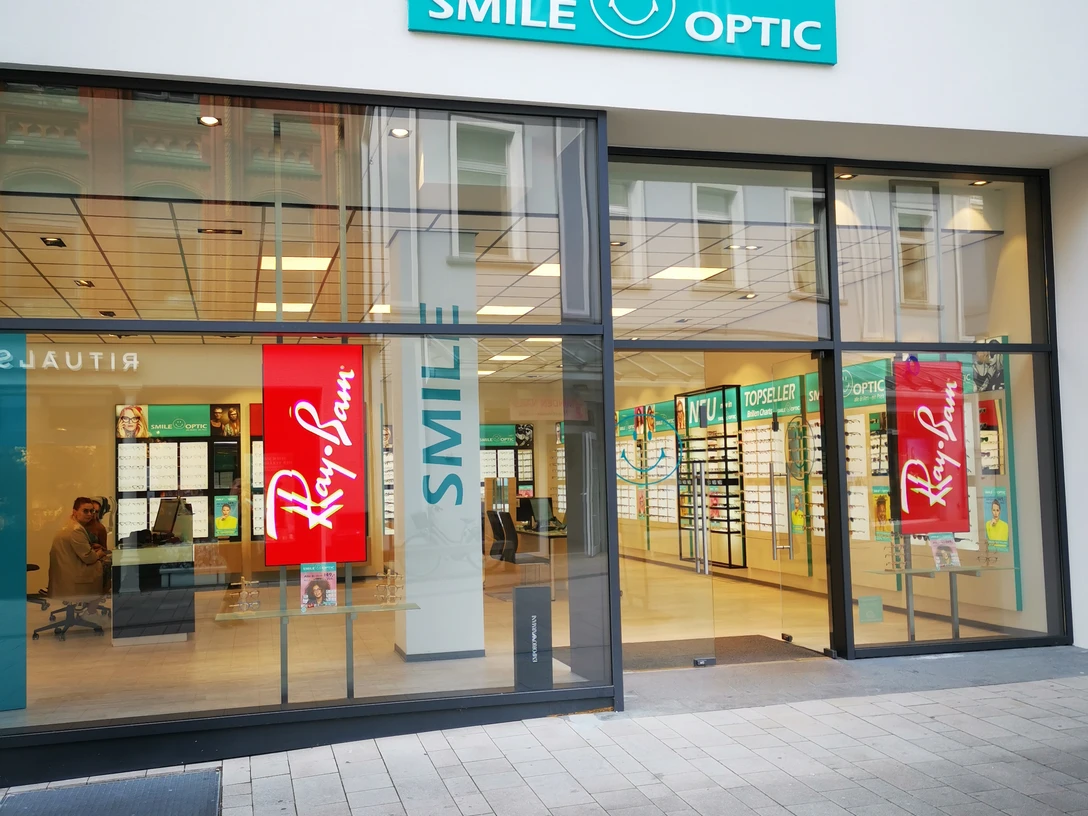Ein modernes Augenoptikfachgeschäft mit großen Glasfenstern und leuchtendem Smile Optic Logo.