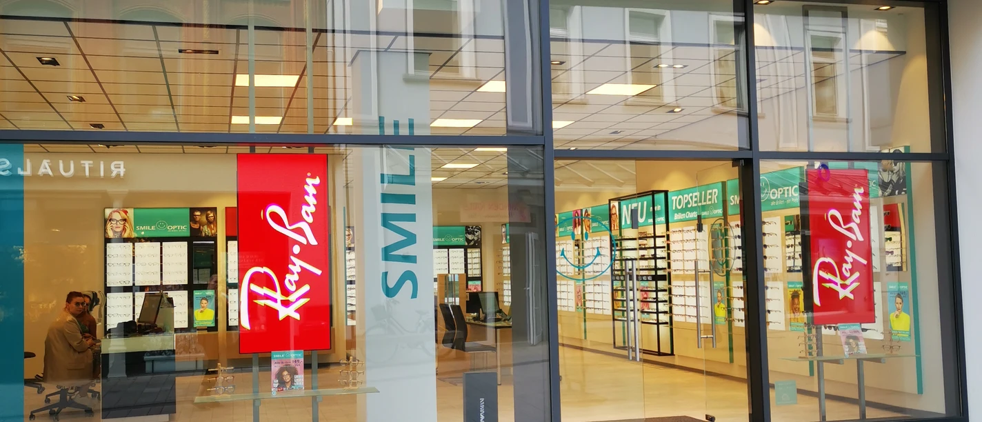Ein modernes Augenoptikfachgeschäft mit großen Glasfenstern und leuchtendem Smile Optic Logo.