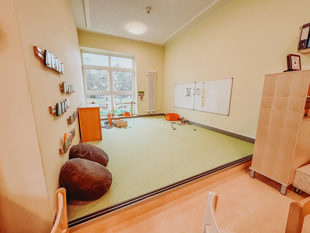 Kindergarten-Rehlingen-2024 (2).jpg Helle Spielecke im Kindergarten Rehlingen mit grünem Teppichpodest, Sitzkissen und Whiteboard.