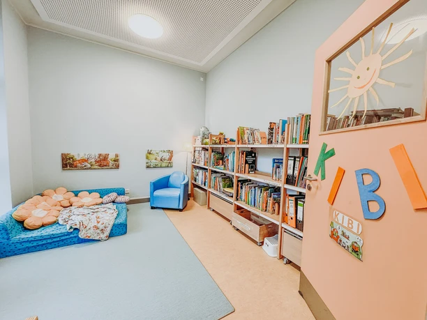 Kindergarten-Rehlingen-2024 (3).jpg Leseecke im Kindergarten mit blauer Matratze, vollen Bücherregalen und bunter Türbeschriftung.