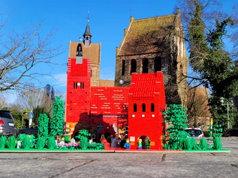 bricks-am-meer-kirche.jpg Rote Backsteinkirche mit passendem LEGO-Modell im Vordergrund, umgeben von Bäumen und Autos.