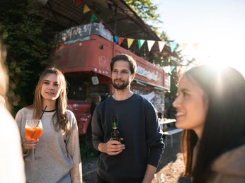 Odonien Eine Gruppe junger Menschen steht vor einem roten Doppeldeckerbus in einer entspannten, urbanen Atmosphäre.A group of young people stand in front of a red double-decker bus in a relaxed, urban atmosphere.