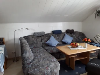 Wohnzimmer Ferienwohnung 1 mit Ecksofa und Kissen, Holztisch, Dachschräge weiß vertäfelt