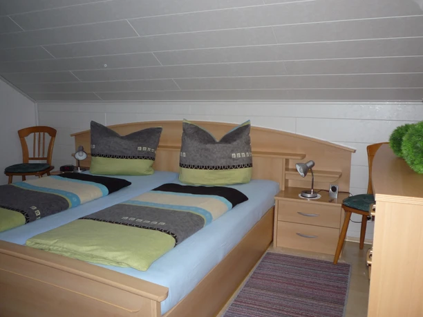 Fewo I, Schlafzimmer Schlafzimmer mit Doppelbett aus Holz, zwei Nachtschränken mit jeweils einer Leselampe, links und rechts vom Bett ein Holzstuhl, rechts eine Kommode