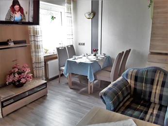 Wohnzimmer Ferienwohnung II mit Sofa in blau-beige, gedeckter Tisch mit vier Polsterstühlen, links ein Sideboard und Regal