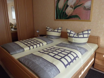 Schlafzimmer der Ferienwohnung II mit Doppelbett aus Holz, zwei Nachttischkommoden, Leselampe, rechts Kleiderschrank mit Spiegeltür