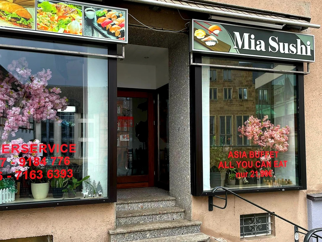 Mia Sushi.jpg Eingang von Mia Sushi mit asiatischen Dekorationen und großem Fenster im urbanen Umfeld.