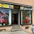 Mia Sushi.jpg Eingang von Mia Sushi mit asiatischen Dekorationen und großem Fenster im urbanen Umfeld.