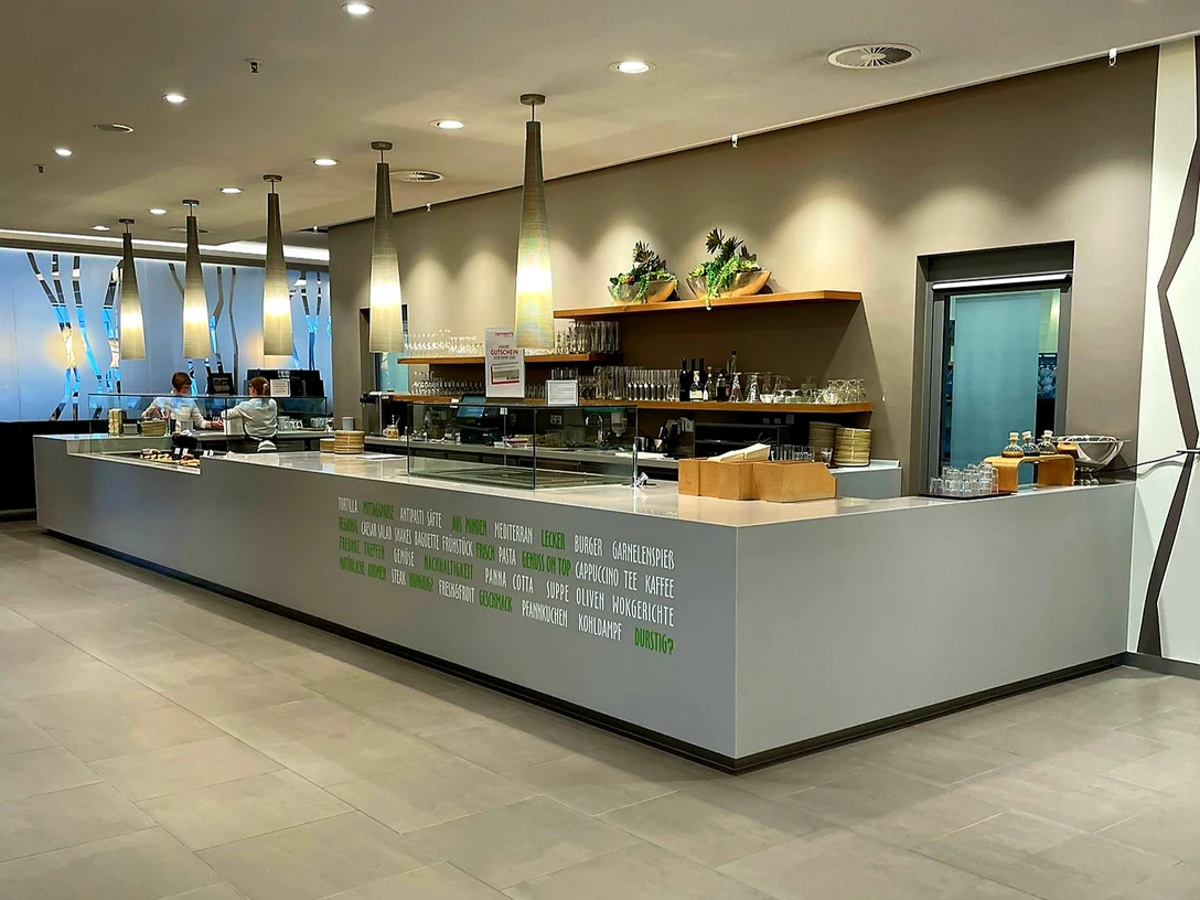 Langes modernes Café-Theken-Setup mit hängenden Lampen, Kaffeemaschinen und eingeräumten Regalen.