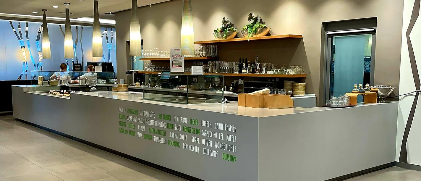 Langes modernes Café-Theken-Setup mit hängenden Lampen, Kaffeemaschinen und eingeräumten Regalen.