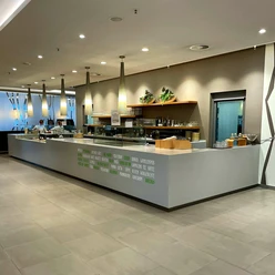 Hermanns.jpg Langes modernes Café-Theken-Setup mit hängenden Lampen, Kaffeemaschinen und eingeräumten Regalen.