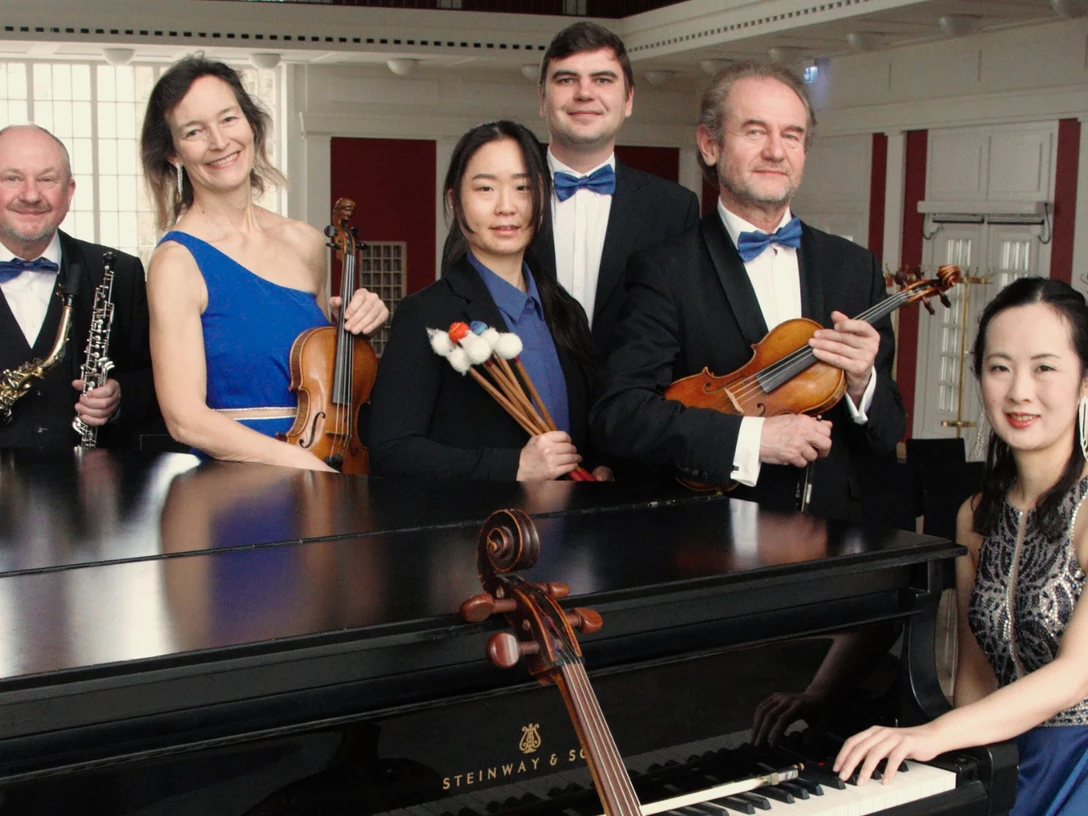 Staatsbad Orchester Eine Gruppe klassischer Musiker in festlicher Kleidung posiert um ein schwarzes Klavier.