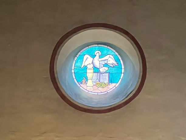Kirchenfenster <p>Rundes Kirchenfenster mit Taube und Olivenzweig in bunter Glasmalerei, symbolträchtige Darstellung.</p>
