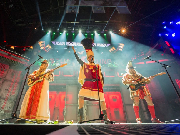 Stunksitzung Three costumed people stand on a stage, illuminated by colorful spotlights.