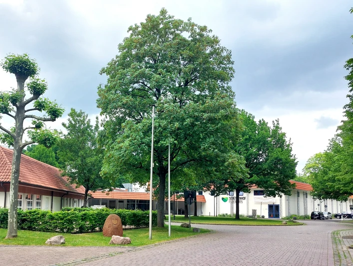 Schützenhof Paderborn Außenansicht Hotelgebäude mit roten Ziegeldächern, umgeben von gepflegten Bäumen und einem gepflasterten Weg.