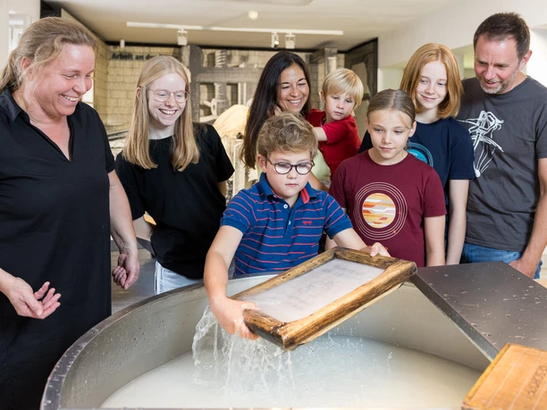 Familie im LVR-Museum Eine Gruppe von Menschen, darunter Kinder und Erwachsene, macht Papier in einem Workshop.