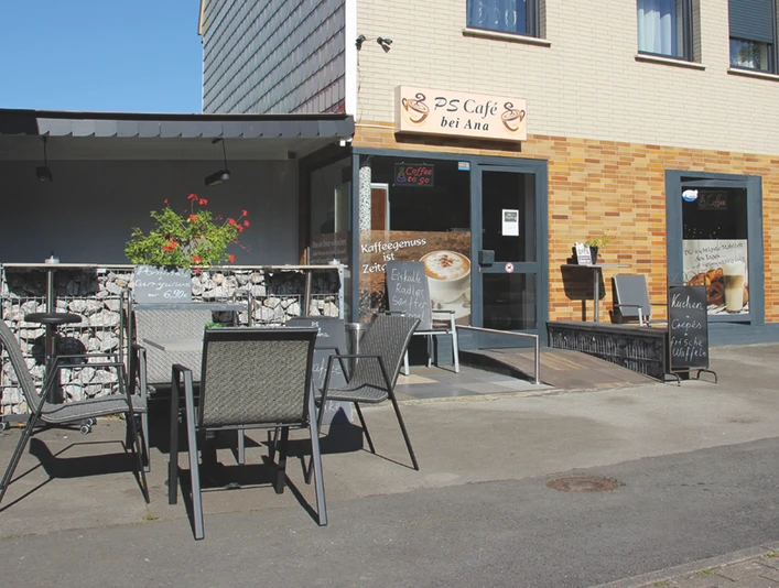 PS Cafe_4448.jpg Ein Café mit Kaffee-Wandgemälde, Außenterrasse und Tischen. Zugang über flache Rampe möglich.