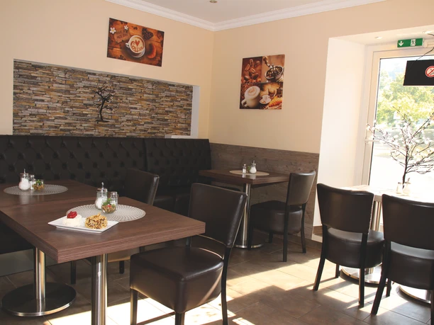 PS Cafe_4459.jpg Gemütliches Café mit modernen Holztischen, Lederstühlen, dekorativen Bildern und hellem Tageslicht.