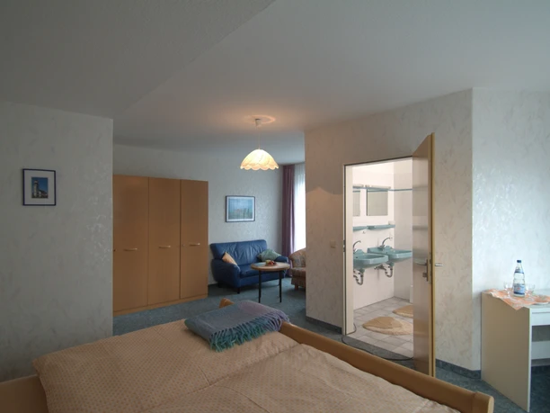 Haus Schwanensee Zimmer.jpg Geräumiges Gästezimmer mit Doppelbett, Kleiderschrank, Sitzecke und eigenem Badezimmerzugang.