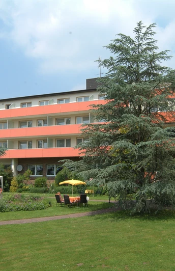 Vierstöckiges Gebäude mit oranger Fassade, umgeben von gepflegtem Garten und grünen Bäumen.