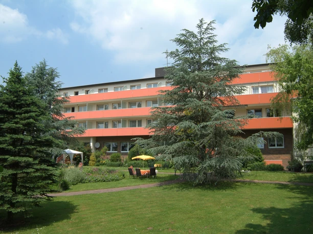 Vierstöckiges Gebäude mit oranger Fassade, umgeben von gepflegtem Garten und grünen Bäumen.