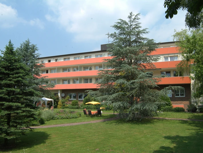 Vierstöckiges Gebäude mit oranger Fassade, umgeben von gepflegtem Garten und grünen Bäumen.