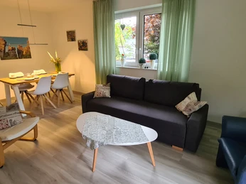 Moderner Wohnbereich mit grauem Sofa, Sessel und Esstisch für vier Personen in heller Atmosphäre.