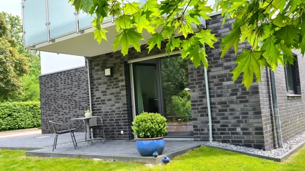FeWo am Park Außenansicht.jpg Moderne Ferienwohnung mit dunkler Klinkerfassade, Terrasse und Gartenmöbeln in grüner Umgebung.