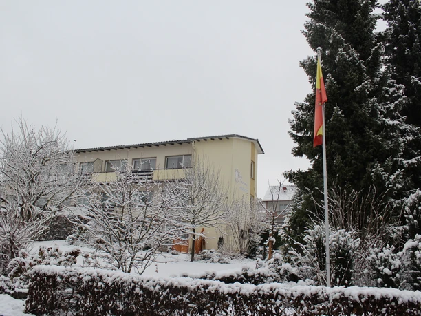 Ein zweistöckiges Haus mit gelber Fassade, umgeben von schneebedeckten Bäumen und Sträuchern.