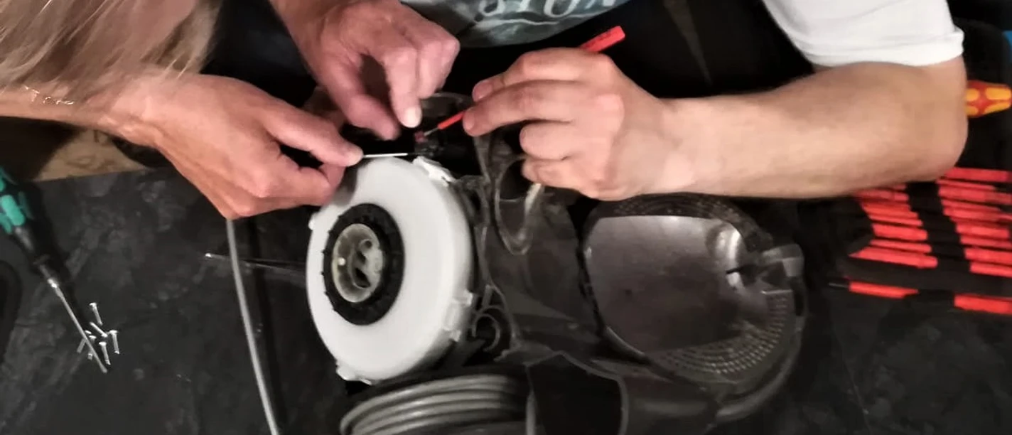 Reparatur Cafe Stemwede Zwei Personen reparieren gemeinsam ein Haushaltsgerät, umgeben von Werkzeug auf einem Tisch.