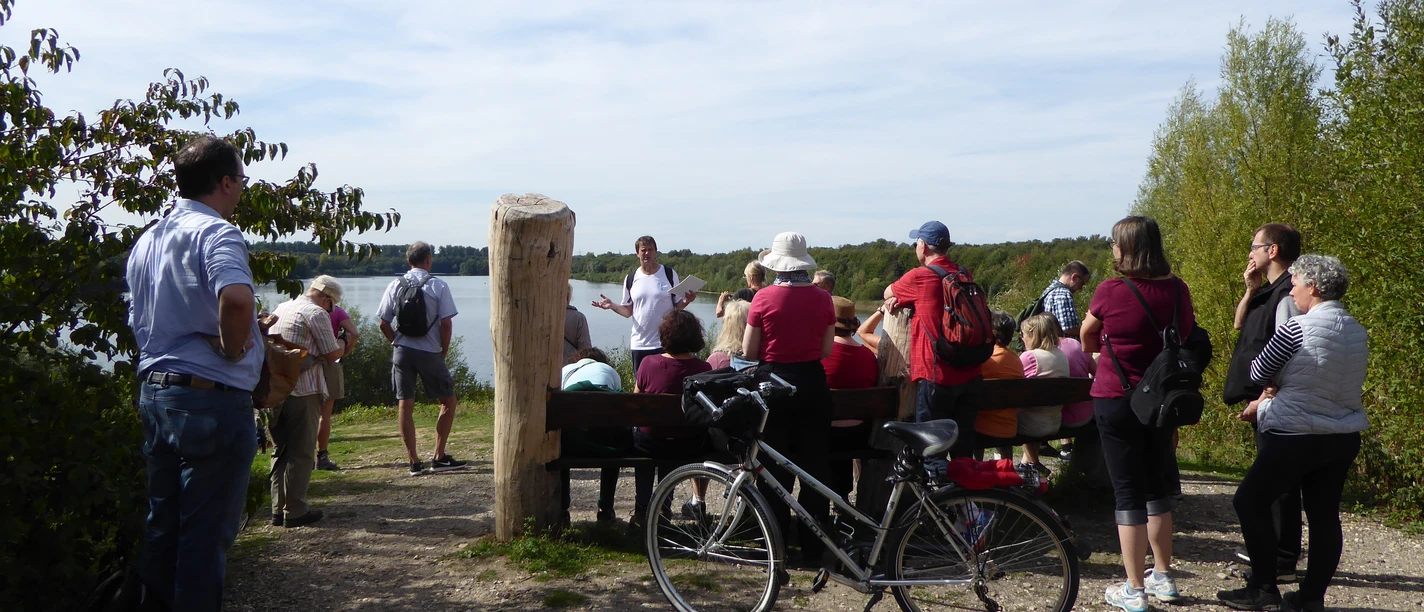Auf dem WasserWeg am Elbsee Gruppe von Menschen hört einem Vortrag am Elbsee zu; im Vordergrund ein geparktes Fahrrad.