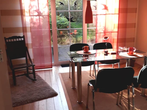 FeWo an den Externsteinen Essbereich.jpg Essbereich mit modernem Glastisch, sechs Stühlen, bodentiefen Fenstern und roten Vorhängen.