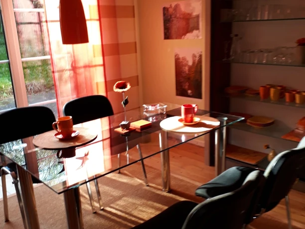 Essbereich mit Glastisch, schwarz gepolsterten Stühlen, orangen Akzenten und natürlichem Lichteinfall.