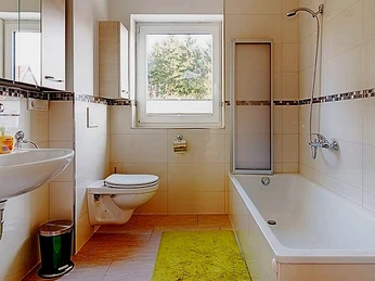 FeWo Herbert Badezimmer.jpg Ein modernes Badezimmer mit Duschbadewanne, WC, Waschbecken und Fenster für natürliches Licht.