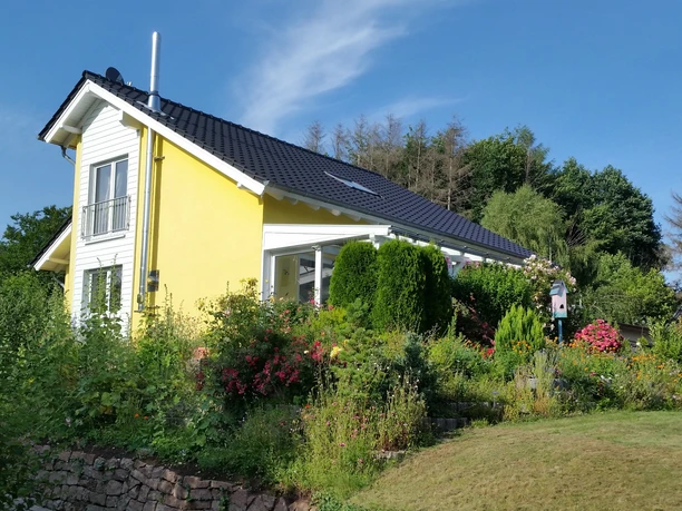FeWo Herbert Außenansicht.jpg Zweistöckiges gelbes Ferienhaus mit Satteldach, umgeben von gepflegtem Garten und grünen Bäumen.