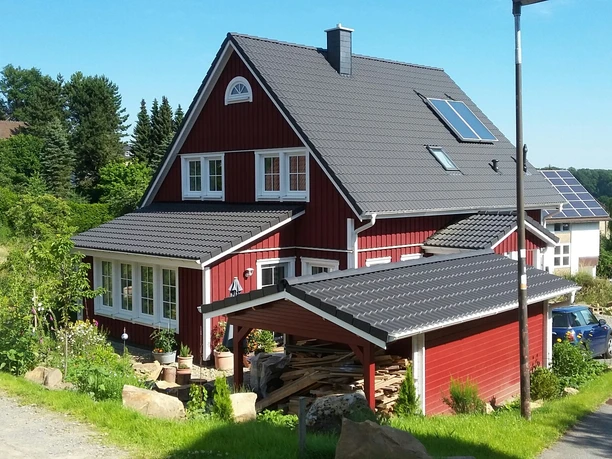 Haus Nordlicht Außenansicht.jpg Ein rotes Holzhaus mit grauem Dach steht inmitten grüner Bäume und Sträucher in einer ruhigen Gegend.