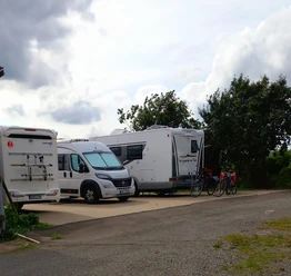 Wohnmobilstellplatz mit zwei geparkten Wohnmobilen, Fahrräder angelehnt, bewölkter Himmel im Hintergrund.