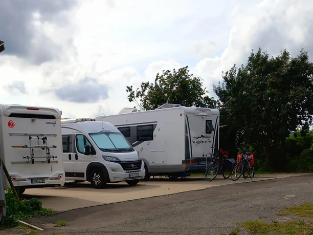 Wohnmobilstellplatz mit zwei geparkten Wohnmobilen, Fahrräder angelehnt, bewölkter Himmel im Hintergrund.
