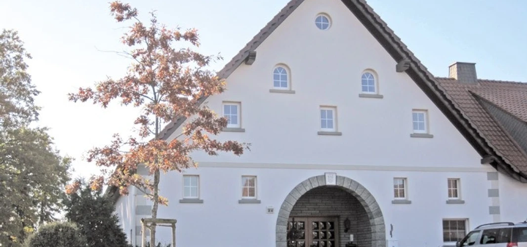 ahlsen-reineberg-altes-amtshaus.jpg Historisches Fachwerkhaus mit markantem Giebel, flankiert von einem jungen Baum und geparktem Auto.