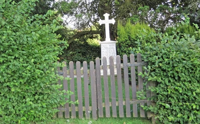 ahlsen-reineberg-privatfriedhof-01.jpg Ein kleiner, von grünen Büschen umgebener Friedhof mit einem Holzzaun und einem weißen Kreuzgrabstein.