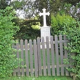 ahlsen-reineberg-privatfriedhof-01.jpg Ein kleiner, von grünen Büschen umgebener Friedhof mit einem Holzzaun und einem weißen Kreuzgrabstein.