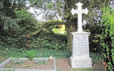 ahlsen-reineberg-privatfriedhof-02.jpg Alter Familienfriedhof mit steinernem Kreuzdenkmal, umgeben von Bäumen und dichtem Laubwerk.