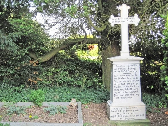 ahlsen-reineberg-privatfriedhof-02.jpg Alter Familienfriedhof mit steinernem Kreuzdenkmal, umgeben von Bäumen und dichtem Laubwerk.