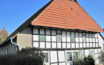 ahlsen-reineberg-domaenenschaeferei-02.jpg Fachwerkhaus mit rotem Ziegeldach und grünen Fensterläden vor strahlend blauem Himmel und Herbstlaub.