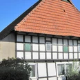 ahlsen-reineberg-domaenenschaeferei-02.jpg Fachwerkhaus mit rotem Ziegeldach und grünen Fensterläden vor strahlend blauem Himmel und Herbstlaub.