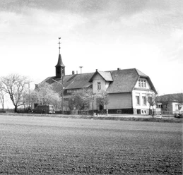 broederhausen-schule-broederhausen-alt.jpg Eine historische Schule mit einem Glockenturm, umgeben von kahlen Bäumen auf einem weiten Feld.